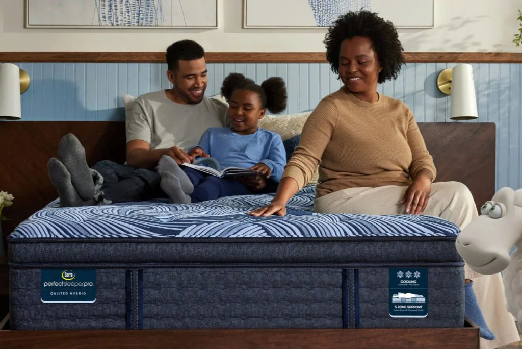 A family relaxes together on a comfortable mattress, enjoying a storybook. A father and daughter smile while a mother watches, creating a cozy, joyful atmosphere in their bedroom, featured in the Serta $500 Sweepstakes