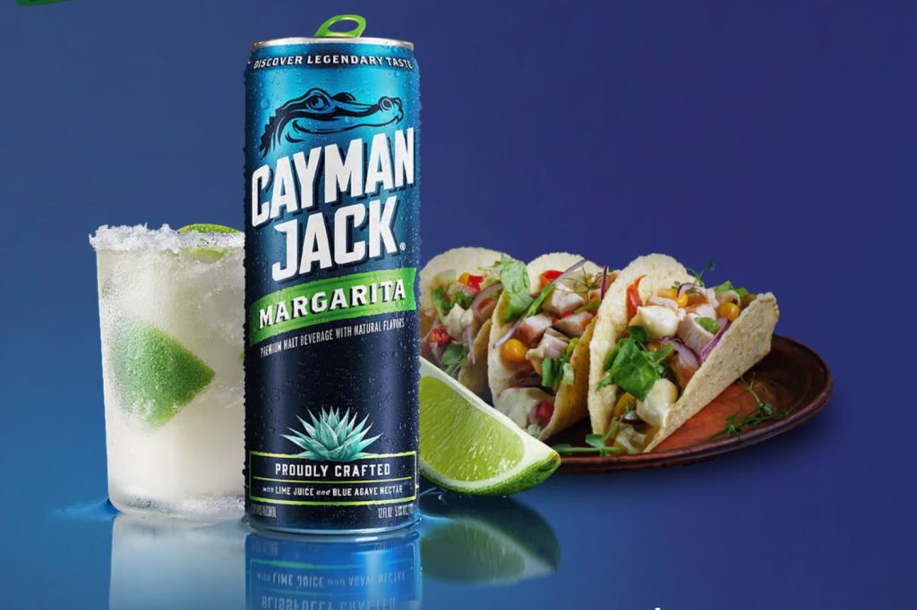 A refreshing margarita in a salted glass alongside three vibrant tacos filled with fresh ingredients, all set against a smooth blue background, featured in the Cayman Jack Instant Win Sweepstakes