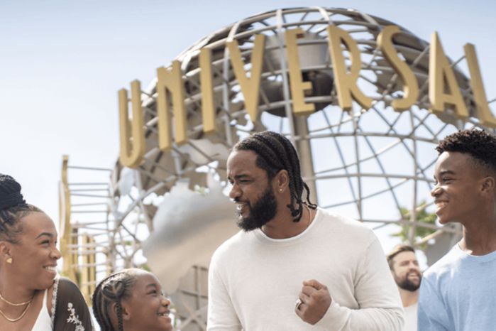 A joyful family stands together in front of a large globe sculpture, smiling and engaging in conversation, enjoying their time at an amusement park, featured in the Visa Universal Studios Hollywood Trip Sweepstakes