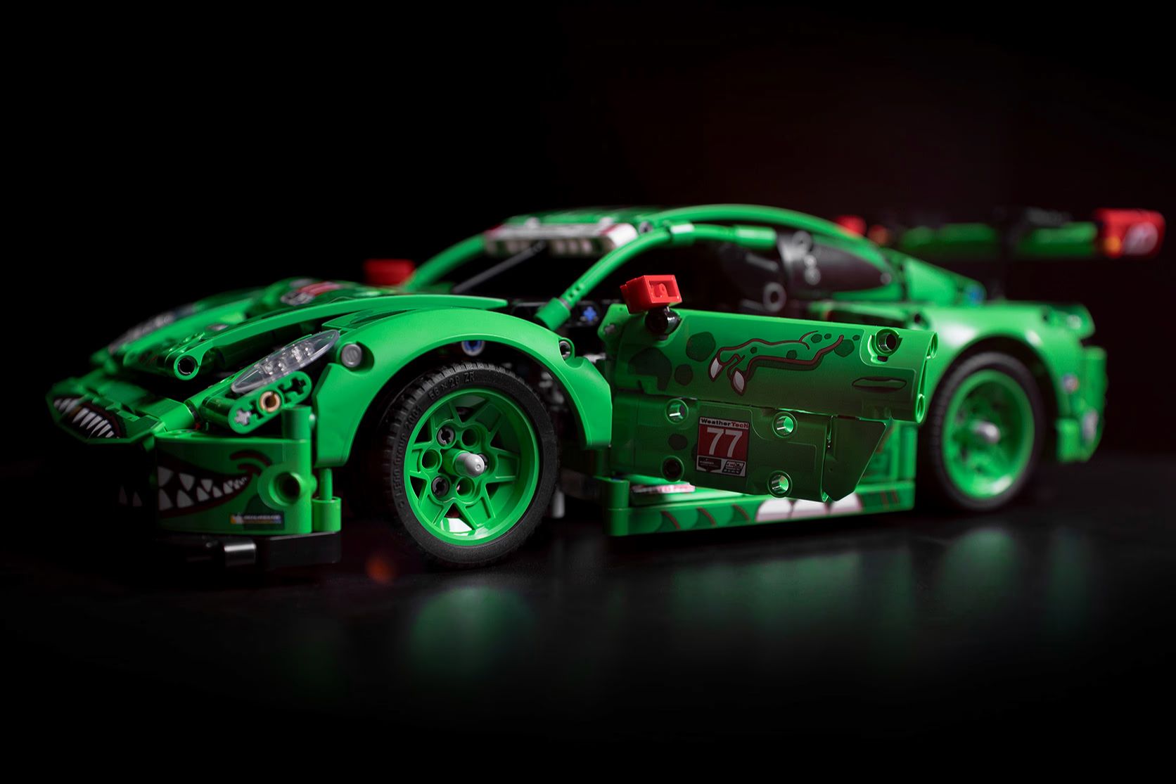 A vibrant green toy race car with intricate designs is showcased on a dark surface, highlighting its sleek body, detailed wheels, and open doors, emphasizing its dynamic racing aesthetic, featured in the Mobil 1 LEGO Porsche Sweepstakes