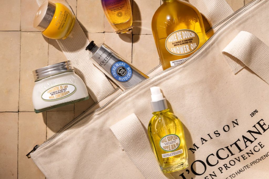 A collection of various skincare products, including creams and oils, arranged on a light-colored surface, with a tote bag showcasing organized beauty essentials, featured in the L'Occitane $504 Best Sellers Sweepstakes