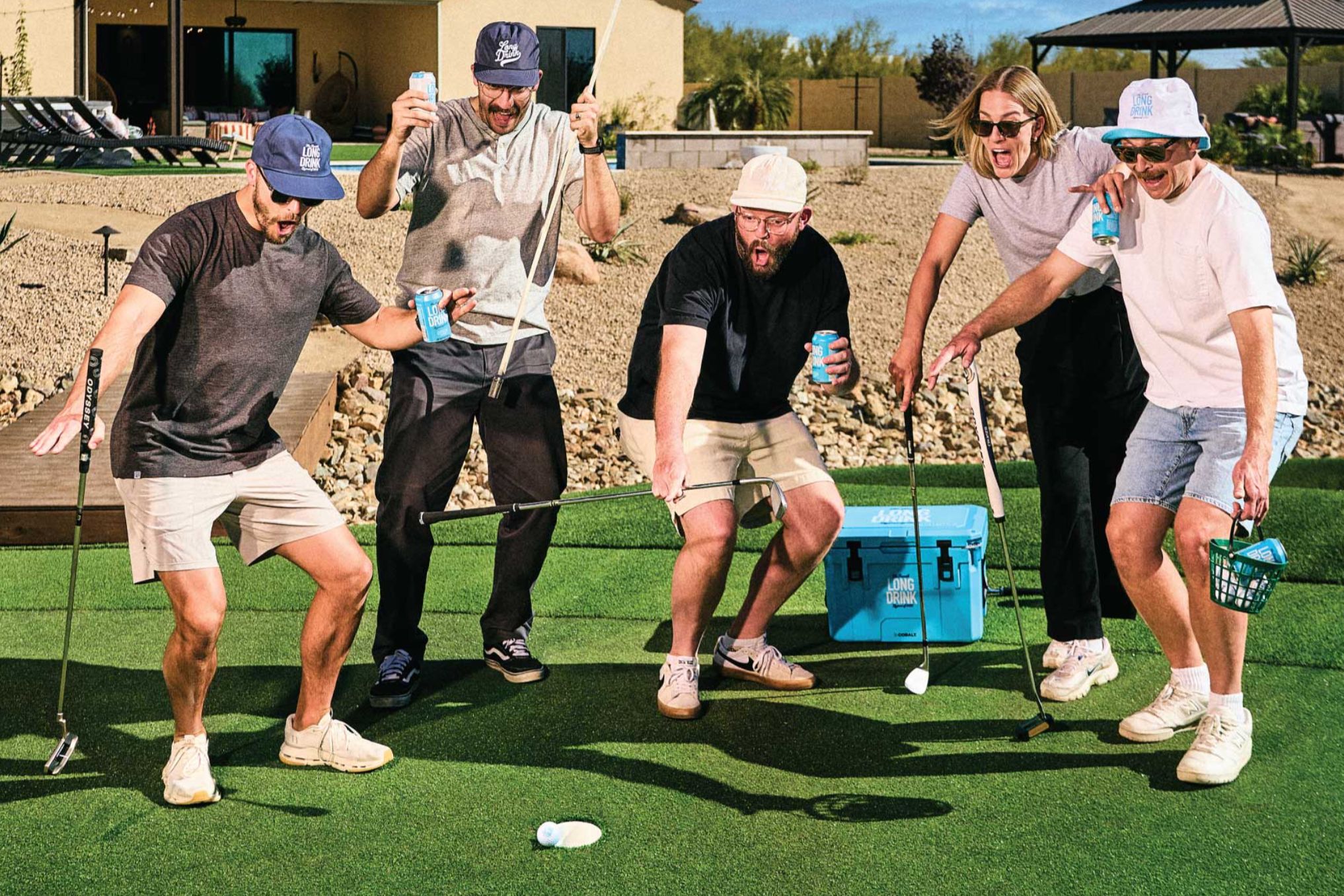 A group of five friends enjoys a playful moment outdoors, laughing and celebrating as they play golf on a green artificial turf, with drinks in hand and a cooler nearby, featured in the Long Drink Golf Giveaway Sweepstakes