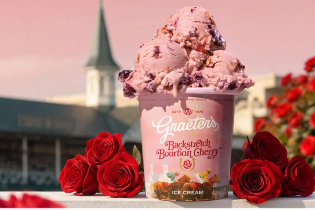 A vibrant scoop of cherry ice cream overflows from a patterned tub, adorned with fresh red roses, set against a serene background with soft pink hues, featured in the Graeter's Year of Ice Cream Derby Giveaway