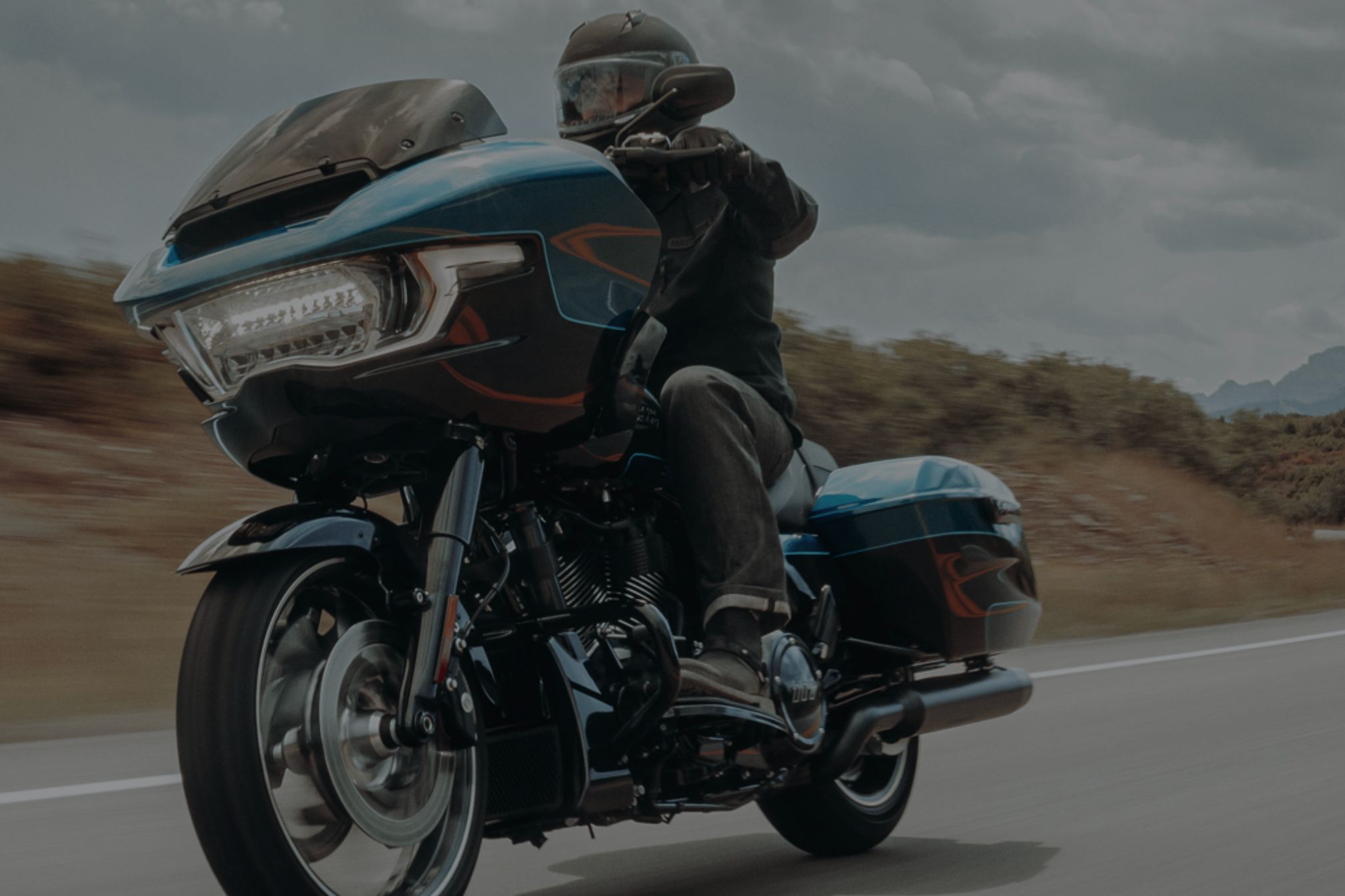 A rider in a black jacket and helmet speeds along a winding road on a sleek blue motorcycle, showcasing a dynamic blend of adventure and power against a scenic backdrop, featured in the Mighty Loud Harley Davidson Sweepstakes