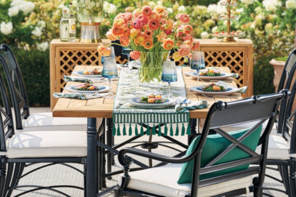 A beautifully set outdoor dining table features a vibrant floral centerpiece, elegant plates, and glassware, surrounded by lush greenery, ideal for an inviting meal, featured in the Frontgate $10K Gift Card Sweepstakes