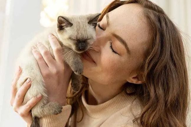 A young woman lovingly hugs a fluffy kitten close to her cheek, sharing a warm and joyful moment in a bright, cozy environment, featured in the PrettyLitter Adoption Fee Reimbursement Sweepstakes