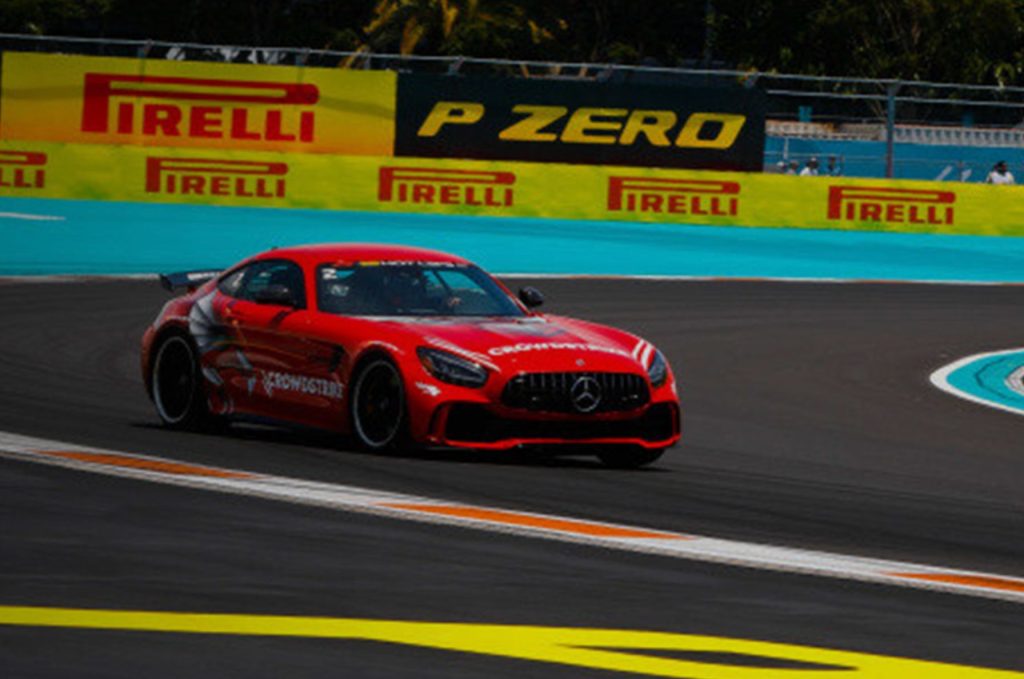 A red Mercedes sports car races around a curved track, showcasing speed and agility. Vibrant banners are visible in the background, enhancing the dynamic atmosphere of the scene, featured in the Pirelli Hot Laps Miami Sweepstakes