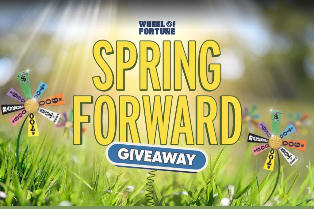 Colorful spinning wheel with cash prizes stands amid bright green grass, illuminated by sunlight, inviting participants to join a spring-themed giveaway event, featured in the Wheel of Fortune Cash Sweepstakes