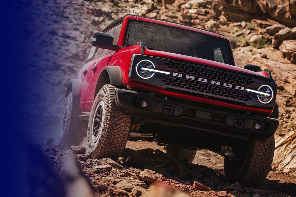 A vibrant red SUV navigates rocky terrain, showcasing its off-road capabilities against a rugged landscape, emphasizing its robust design and adventurous spirit, featured in the Ford Tee-To-Trail Sweepstakes
