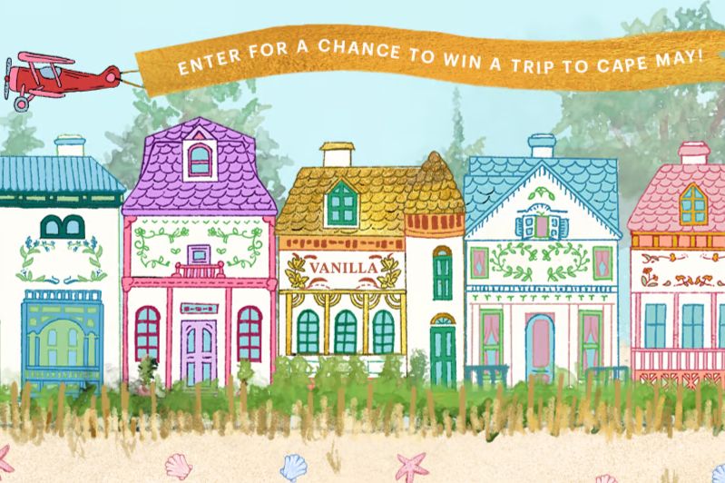 A row of colorful, whimsical houses with various architectural designs sits beside a sandy area, while a small red biplane flies above, trailing a banner announcing a contest, featured in the Lenox Golden Winner Getaway Sweepstakes