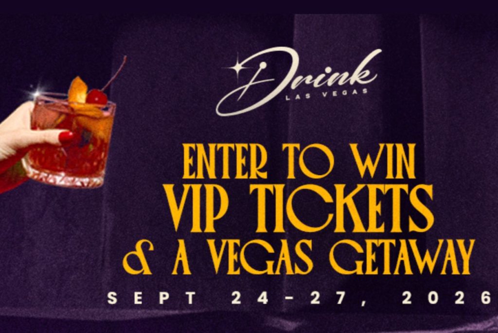 A hand with red nails holds a cocktail glass filled with an amber drink and garnished with a cherry and an orange slice, set against a dark, elegant backdrop, featured in the Drink Las Vegas Sweepstakes 2026