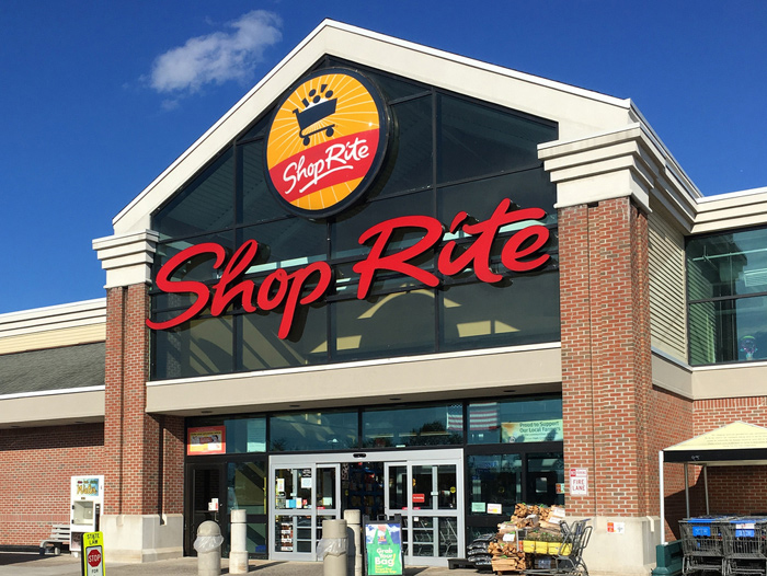 A grocery store entrance features a large glass facade and a bold red sign. Shopping carts are visible outside, under a clear blue sky, featured in the ShopRite $2,500 Sweepstakes