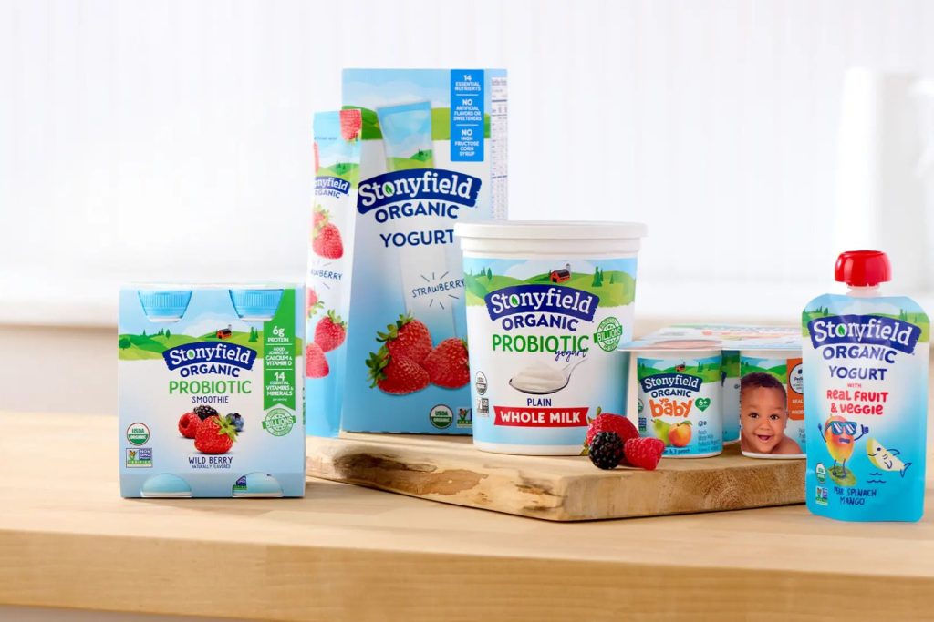 A variety of Stonyfield organic yogurt products are arranged on a wooden surface, including smoothies and pouches, alongside fresh strawberries and blackberries, creating a fresh and inviting scene, featured in the Year of YoBaby Sweepstakes