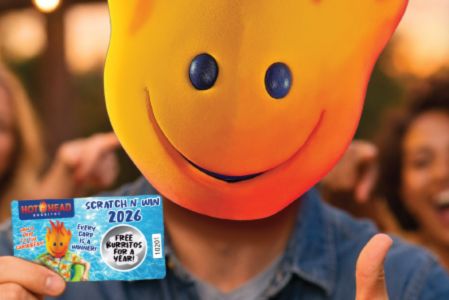 A person wearing a large, smiling orange mask holds a card stating "Free Burritos for a Year," while friends cheer in the background, creating a lively atmosphere, featured in the Hot Head Burritos Caribbean Trip Sweepstakes