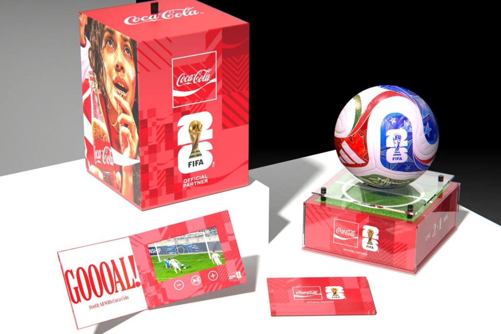 A vibrant display showcasing a FIFA-themed soccer ball on a grass pedestal, paired with a colorful box and a booklet featuring soccer highlights and fan excitement, featured in the Coca-Cola Match Ball Sweepstakes