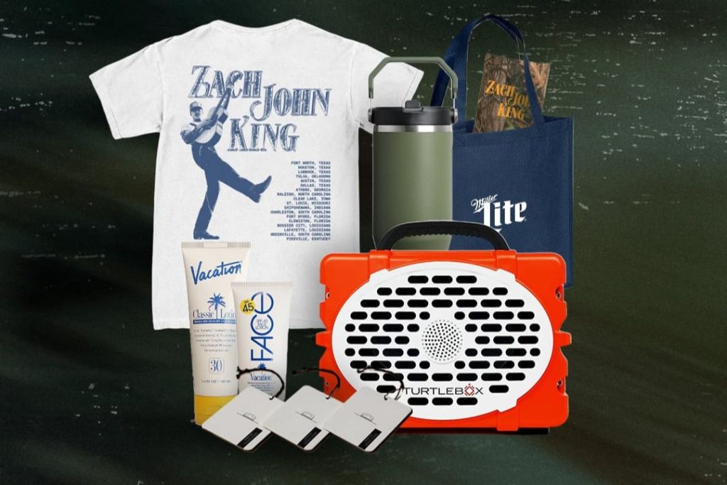 A collection of promotional items includes a t-shirt featuring a performer, sunglasses, sunscreen, a water bottle, a tote bag, and a portable speaker, all arranged against a dark background, featured in the Zach John King Backwoods Bundle Sweepstakes