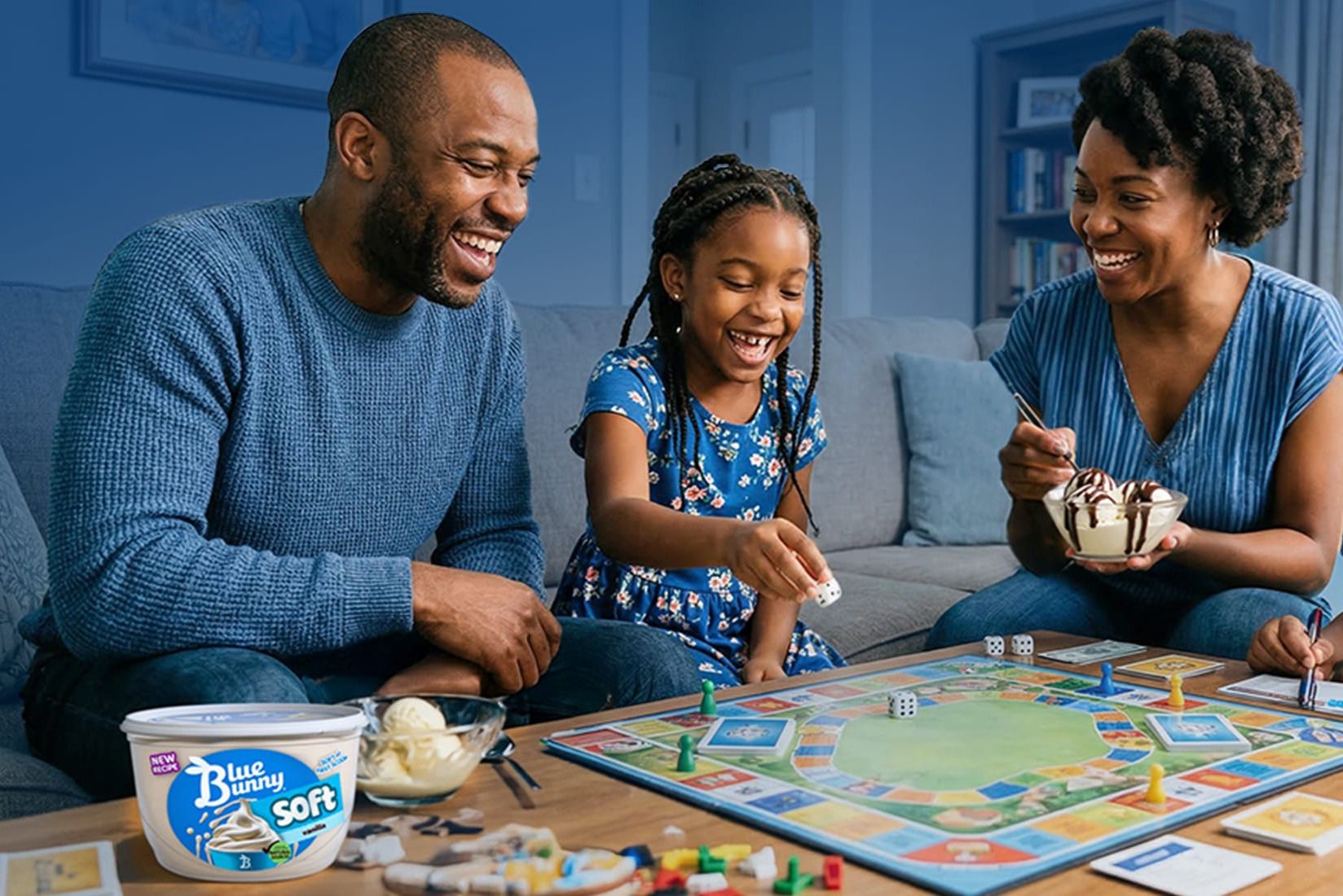 A family enjoys a game night, laughing and playing on a colorful game board, while sharing bowls of ice cream and dice, creating a joyful atmosphere together, featured in the Blue Bunny Family Game Night Sweepstakes