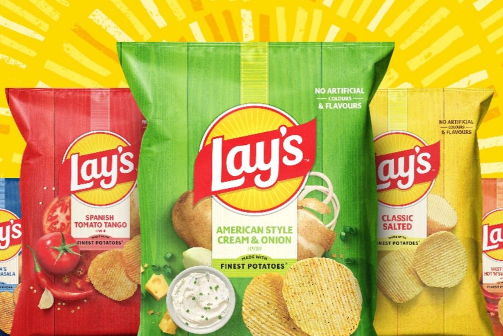 Colorful bags of Lay's potato chips arranged in a semi-circle, showcasing flavors like Spanish Tomato Tango, American Style Cream & Onion, and Classic Salted against a bright yellow background, featured in the Lays Swag Sweepstakes