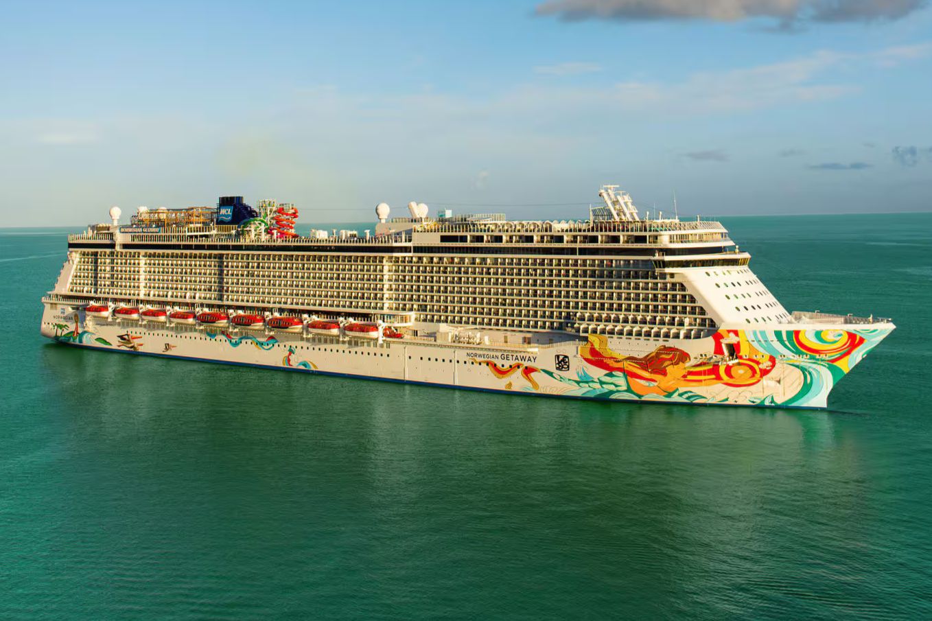 A large cruise ship with a colorful abstract design sails smoothly on calm blue waters under a clear sky, showcasing levels of decks and various attractions, featured in the Elvis Duran Cruise Sweepstakes