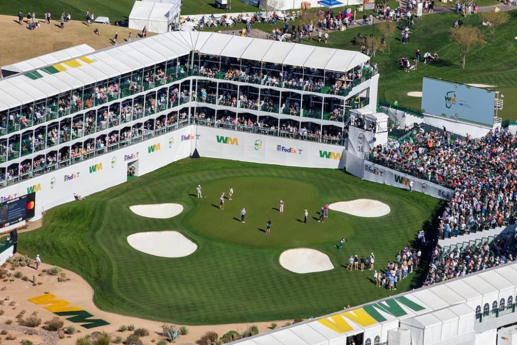 A crowd gathers at a lively golf tournament surrounded by large tents. Players putt on a well-maintained green with spectator areas packed with fans enjoying the event, featured in the WM Recycling Is Real Sweepstakes