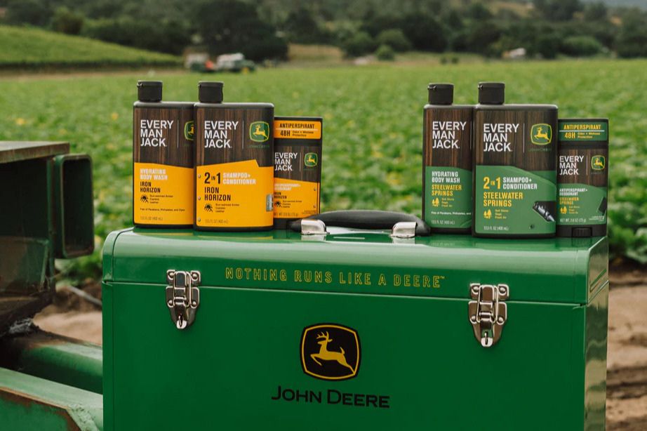 A green toolbox sits on a farm equipment, surrounded by lush fields. Various Every Man Jack personal care products are neatly arranged on top of the toolbox, showcasing their different features, featured in the Every Man Jack John Deere Sweepstakes