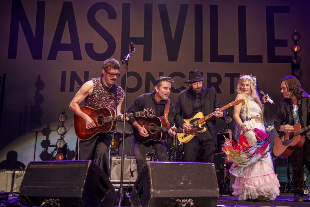 A lively concert scene features five musicians playing guitars on stage, with a female performer in a colorful dress engaging the audience, set against a backdrop highlighting "Nashville.", featured in the Nashville Encore Tour Getaway Sweepstakes