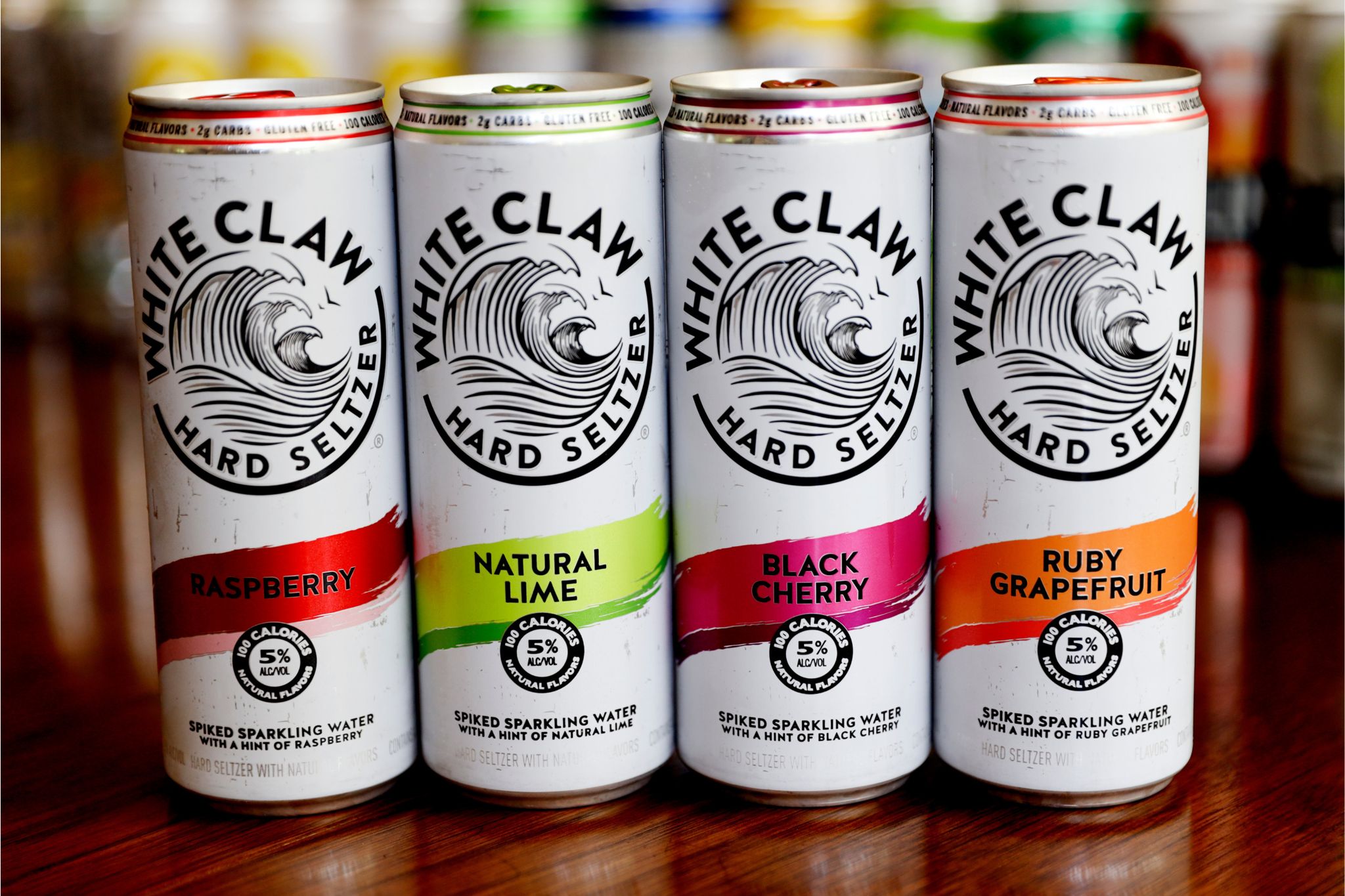 Four cans of hard seltzer are displayed on a wooden surface, showcasing flavors of Raspberry, Natural Lime, Black Cherry, and Ruby Grapefruit, with a refreshing design and vibrant colors, featured in the White Claw Personal Watercraft Sweepstakes