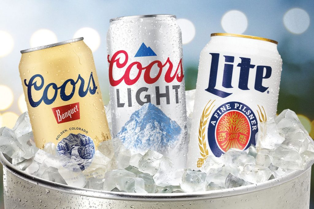 Three beer cans, including Coors Banquet, Coors Light, and Miller Lite, are nestled in ice in a metal bucket, set against a softly blurred background of lights, featured in the Beer & Ice for a Year Sweepstakes