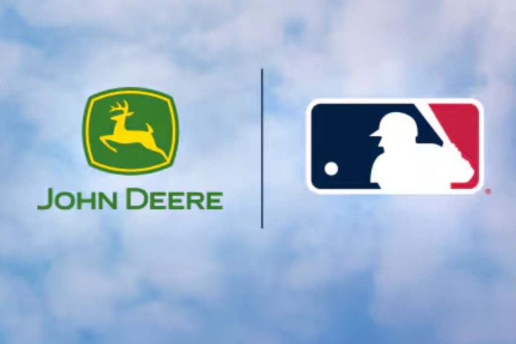 A green and yellow logo of a deer is shown alongside a silhouette of a baseball player in a blue and red rectangular design, set against a light blue cloudy background, featured in the John Deere All-Star Experience Sweepstakes