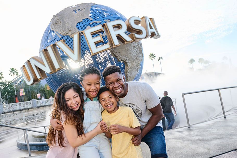 A joyful family of four smiles as they pose together in front of a large globe structure, surrounded by mist, at a famous theme park. The atmosphere is vibrant and lively, featured in the Jersey Shore Sweepstakes 2026