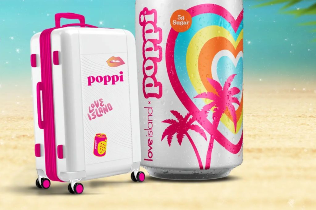 A colorful suitcase with pink accents sits next to an oversized can adorned with vibrant heart and palm tree designs, set against a bright beach backdrop, featured in the Pepsi Fiji Trip Sweepstakes