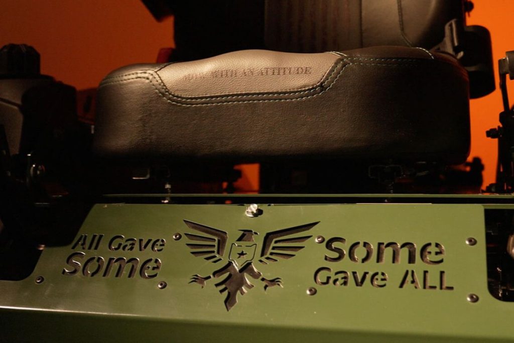A close-up view of a black leather seat on a green machine, featuring engraved text and a decorative eagle emblem, all set against an orange backdrop, featured in the Bad Boy Mowers 2026 Memorial Day Sweepstakes