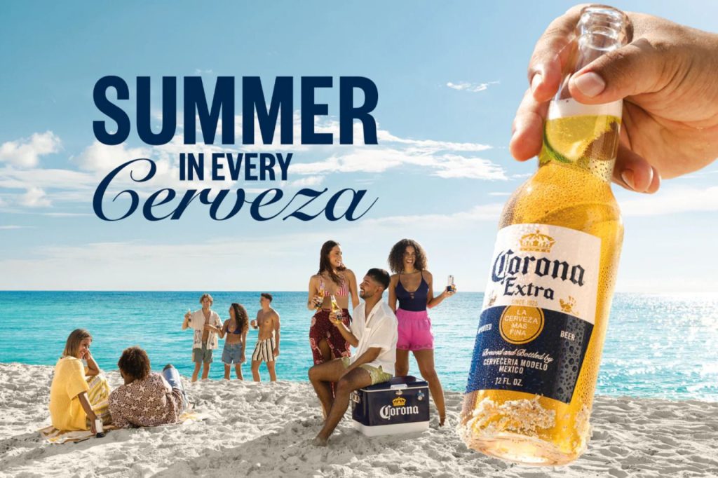 A group of friends celebrates on a sunny beach, enjoying drinks and laughter, with one person holding a cold beer in the foreground, encapsulating a vibrant summer atmosphere, featured in the Corona Beach Getaway Sweepstakes
