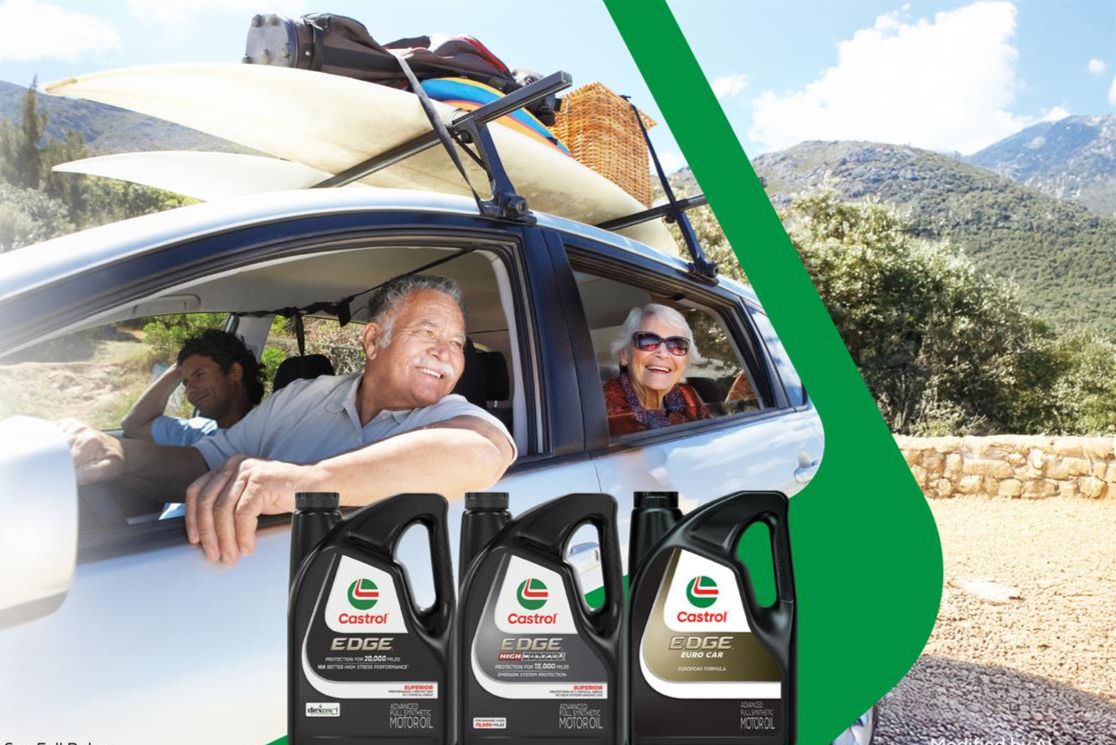 A smiling elderly couple enjoys a scenic drive in a car with outdoor gear on the roof, while nearby are bottles of motor oil positioned prominently, featured in the Castrol $5,000 Sweepstakes