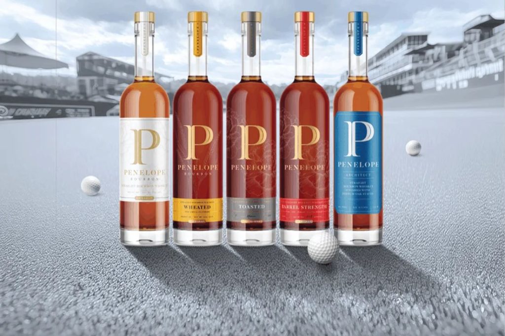 A selection of five bourbon bottles lined up against a blurred golf course backdrop, featuring distinct labels and colors, with a golf ball in the foreground, featured in the Penelope Classic Club Sports Sweepstakes