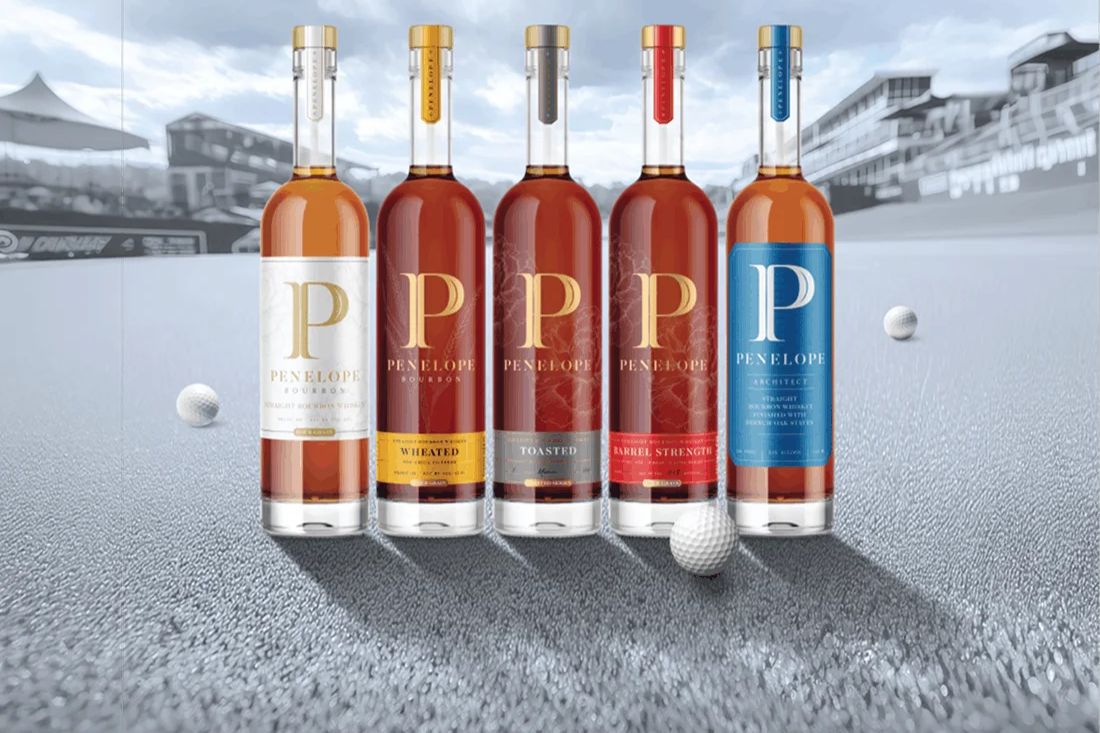 A selection of five bourbon bottles lined up against a blurred golf course backdrop, featuring distinct labels and colors, with a golf ball in the foreground, featured in the Penelope Classic Club Sports Sweepstakes