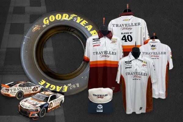 A racing-themed display showcases a Goodyear tire, two racing shirts, a cap, and a model car arranged on a checkered background. The attire features the Traveller brand prominently, featured in the Shop JR Nation Autographed Tire Sweepstakes