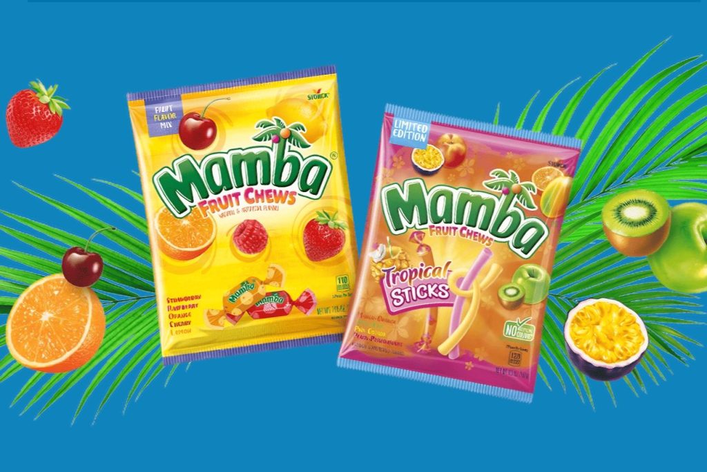 Two colorful packs of Mamba Fruit Chews are displayed against a vibrant blue background, surrounded by tropical fruits like oranges, cherries, and kiwis, featured in the Mamba Sweepstakes