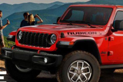 A bright red off-road vehicle parked on rocky terrain, with mountains in the background. Two people are taking photos while another stands nearby, enjoying the scenic view, featured in the Coca-Cola America 250 Hy-Vee Sweepstakes