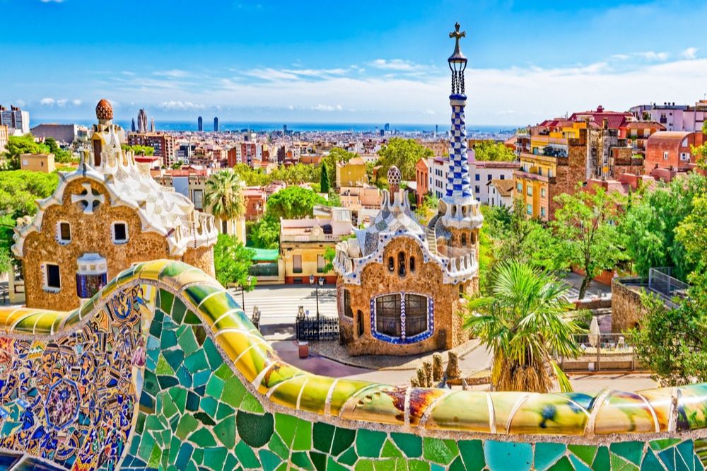 A vibrant view of Parc Güell showcases its colorful mosaic architecture, lush greenery, and the distant skyline of Barcelona against a clear blue sky, featured in the Fresh Del Monte Barcelona Trip Sweepstakes