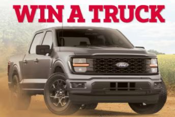 A grey pickup truck is parked on a dirt surface with a scenic background of fields. Dust surrounds the tires, emphasizing the rugged terrain, featured in the Rural King Ford F-150 Sweepstakes