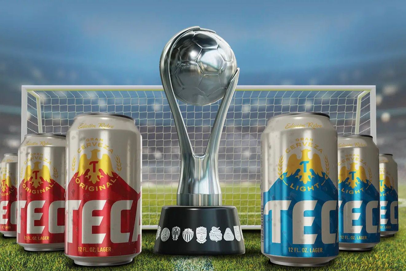 A silver soccer trophy stands in front of a goal, flanked by cans of lager beer. The scene captures a celebratory atmosphere, evoking excitement around soccer, featured in the Tecate Fanatics Gift Card Sweepstakes