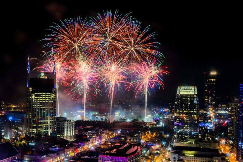 Spectacular fireworks burst in vibrant colors over a city skyline at night, illuminating buildings and streets below, creating a festive atmosphere, featured in the Visit Music City Trip Sweepstakes