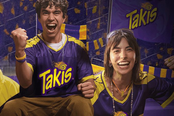 A young man and woman enthusiastically celebrate wearing matching purple jerseys, their expressions joyful and energetic as they cheer on their team, featured in the Takis $5,000 Sweepstakes