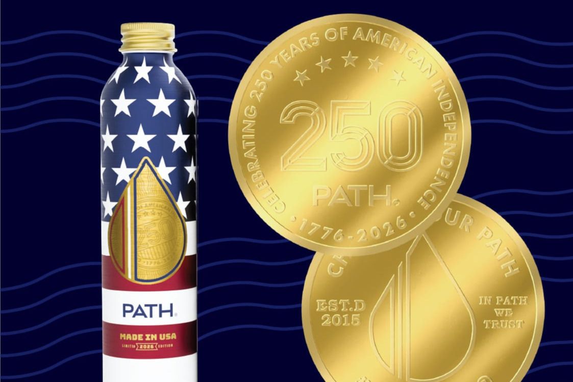 A decorated beverage bottle featuring a stars-and-stripes design stands beside two gold commemorative coins, highlighting an American independence celebration theme with the number 250, featured in the Made In the USA Sweepstakes 2026