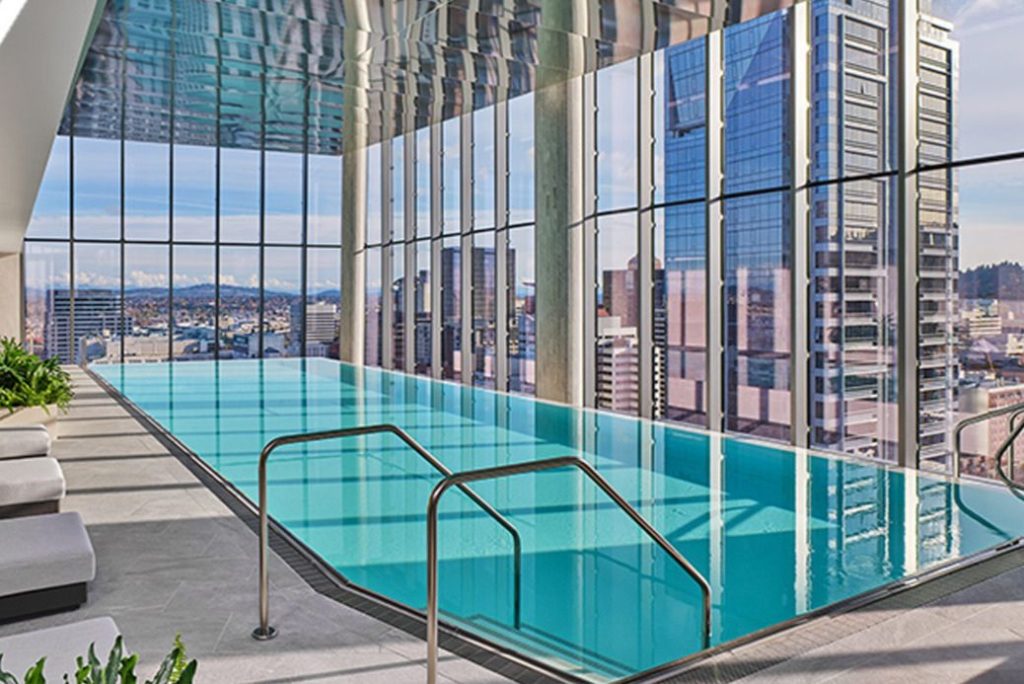 A stunning indoor pool with a sleek design, surrounded by floor-to-ceiling windows showcasing a vibrant city skyline and mountains in the background, featured in the Travel Oregon Portland Escape Sweepstakes