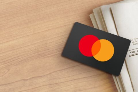 A payment card with a red and yellow logo rests on a wooden table beside a stack of newspapers, featured in the Gift Card Giveaway 2026