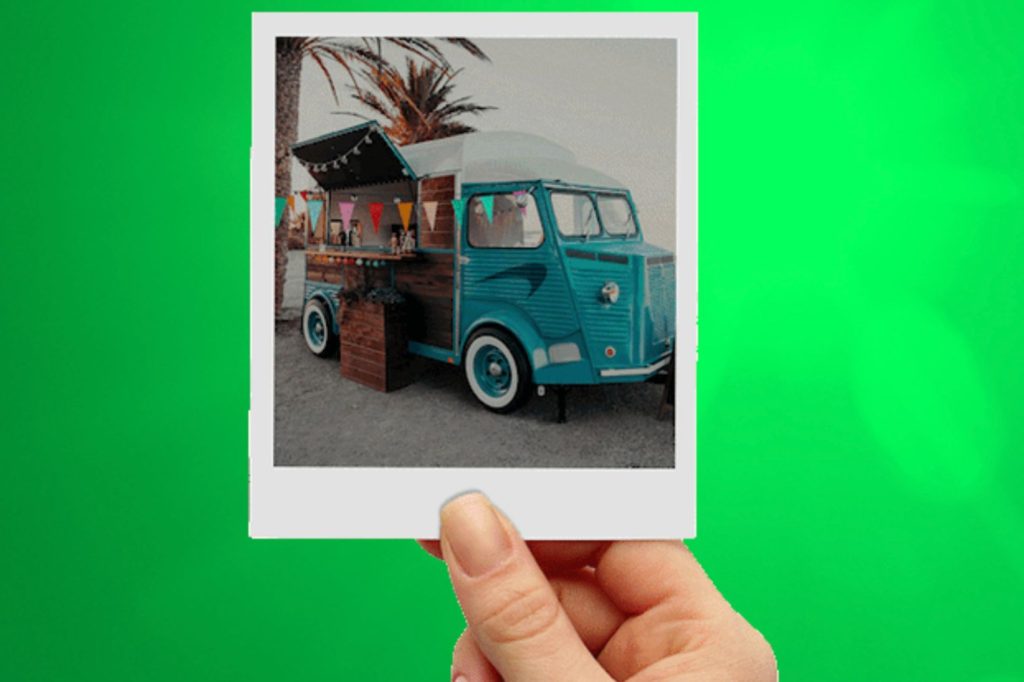 A hand holds a polaroid photo of a colorful food truck with a beachy vibe, decorated with bunting, set against palm trees and a bright background, featured in the Newport $15,000 Sweepstakes