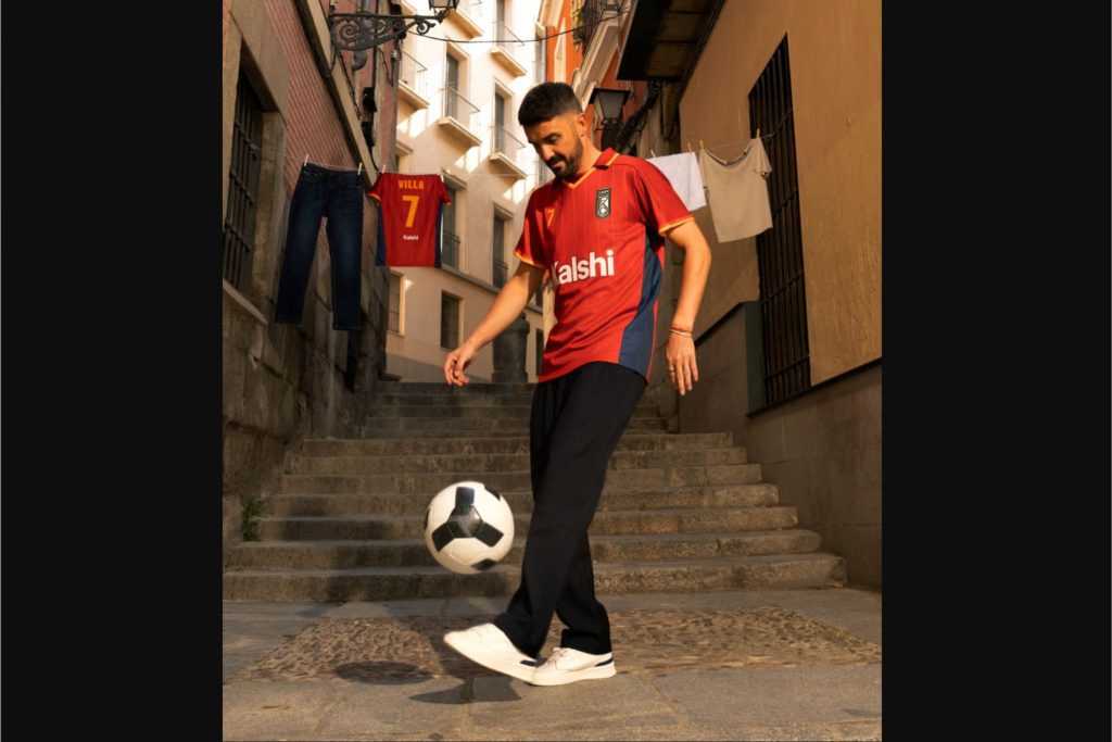 A man in a red jersey skillfully juggles a soccer ball while standing on steps. Clothes are hanging on a line nearby, and the scene captures a vibrant urban atmosphere, featured in the Kalshi $1,000,000 World Cup Sweepstakes