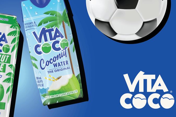 A vibrant blue backdrop features two cartons of coconut water, one prominently displaying palm trees, alongside a black and white soccer ball, featured in the Vita Coco Soccer Sweepstakes